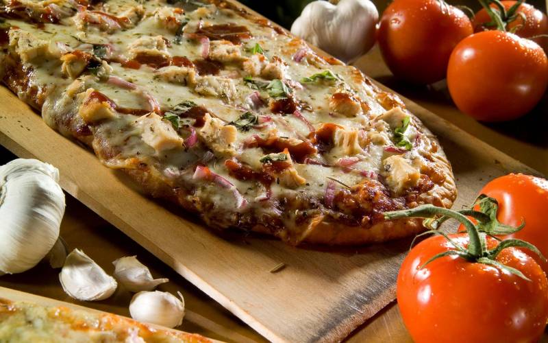 Pizza sortant du four avec tomate et ognons entiers autour